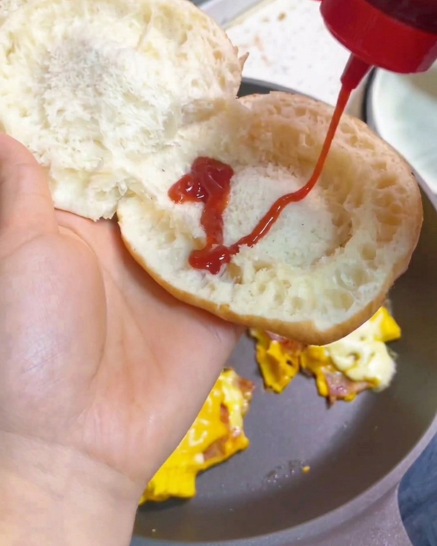 Une main pressant un zigzag de ketchup sur lintérieur dun pain à burger toasté.