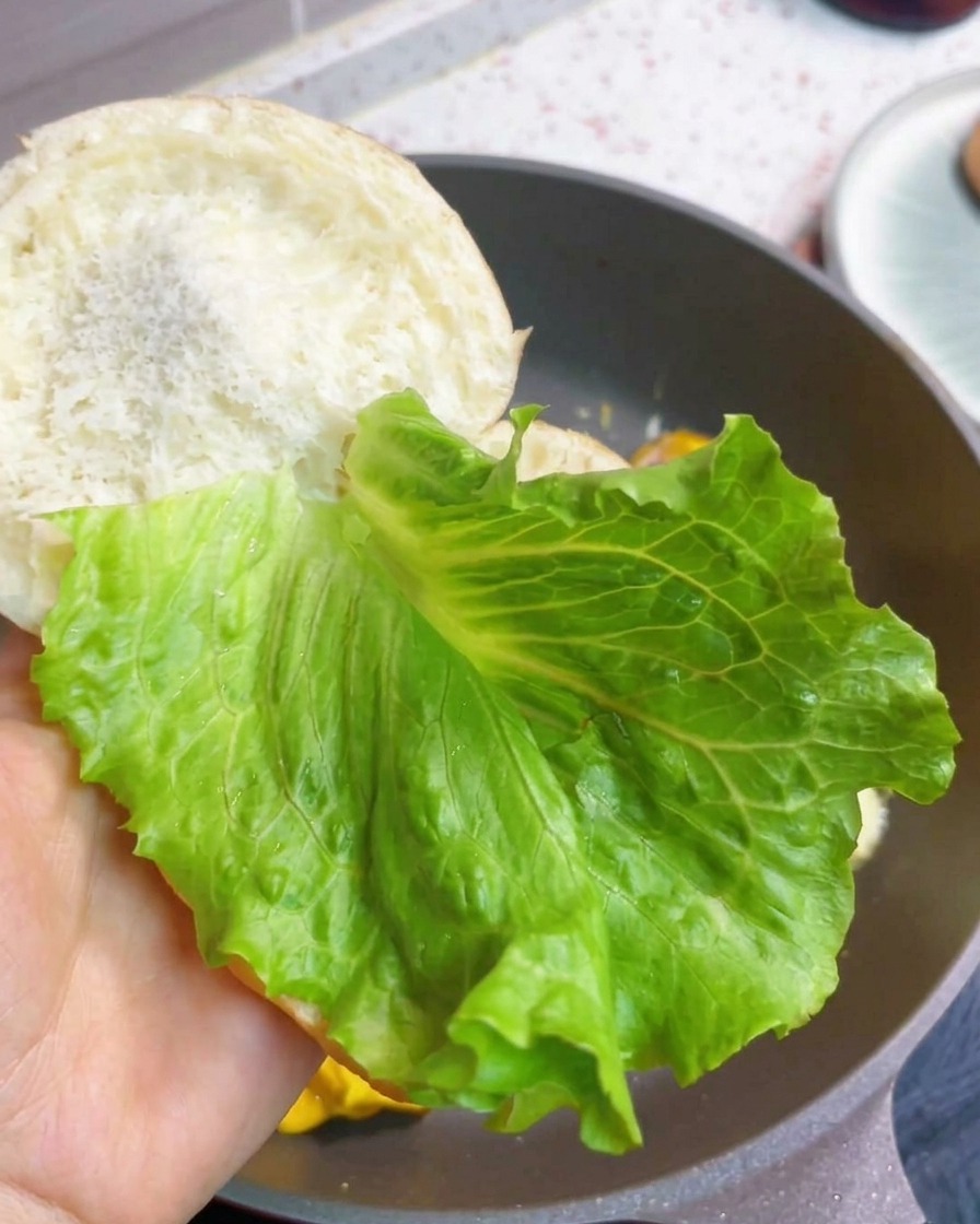 Un burger de petit-déjeuner en cours dassemblage avec de la laitue fraîche et la garniture bacon-œuf-fromage.