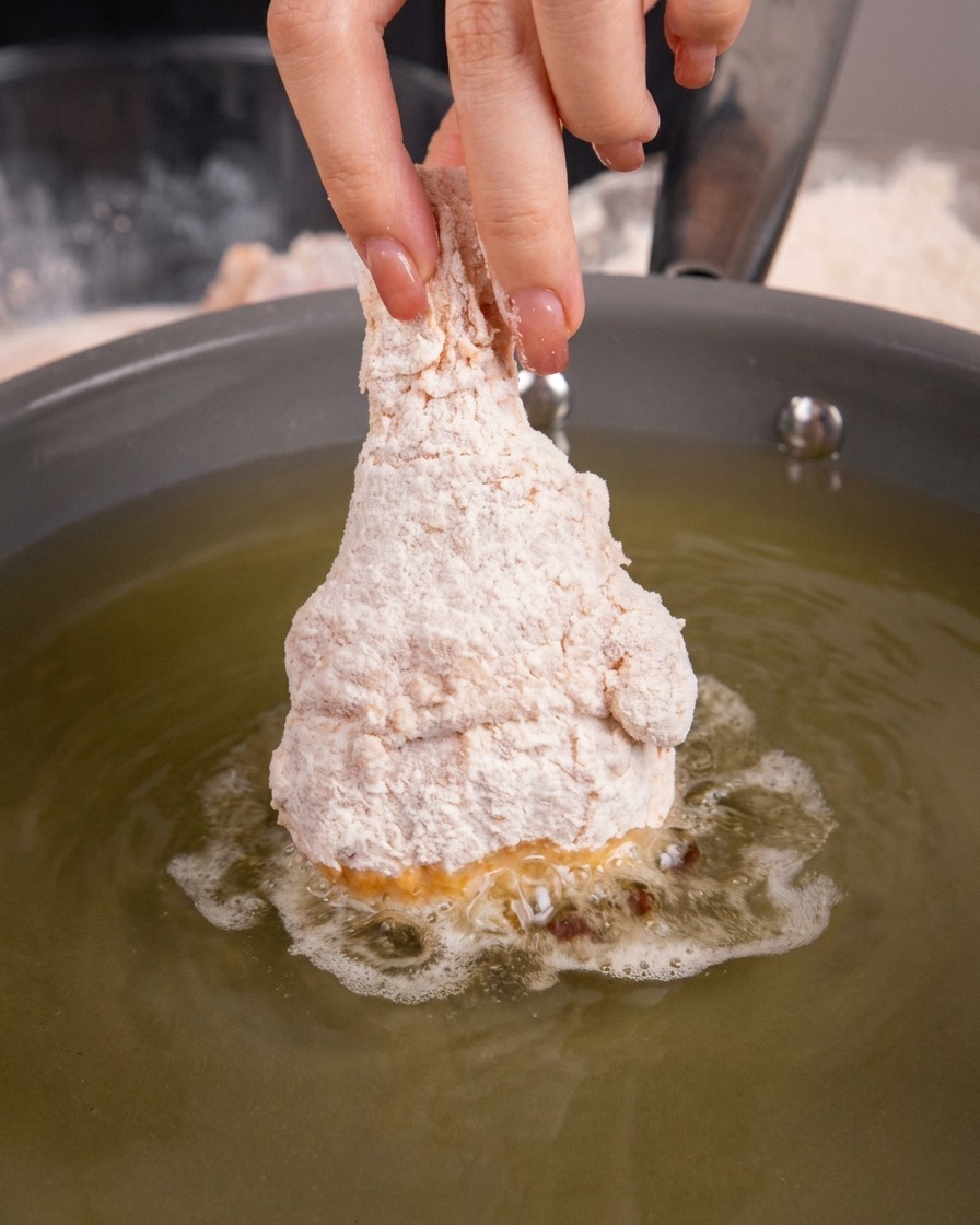 Pilon de poulet cru pané plongé dans lhuile chaude dans une poêle à frire.