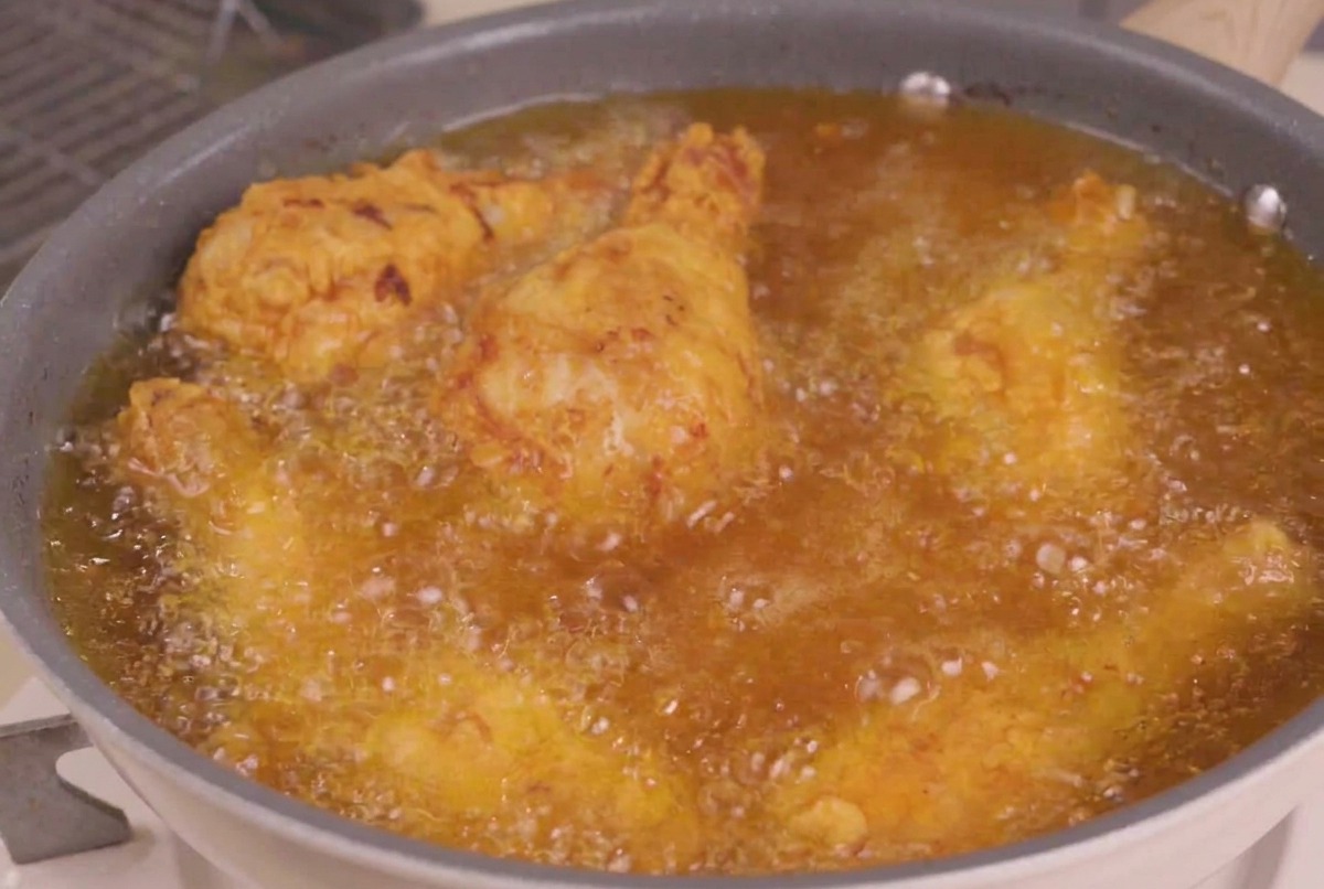 Morceaux de poulet frit replongés dans une poêle dhuile chaude et bouillonnante pour létape finale de friture.