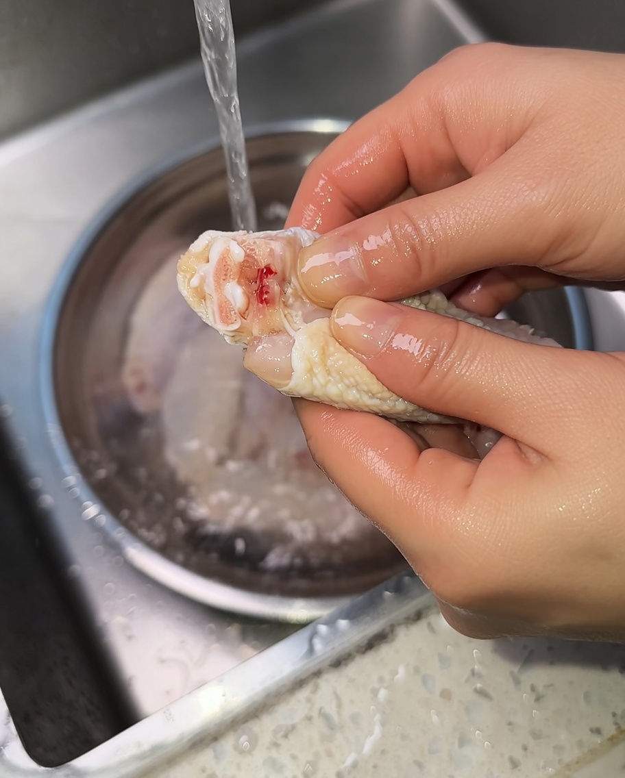 Gros plan de mains pressant une aile de poulet crue pour expulser le sang de larticulation.