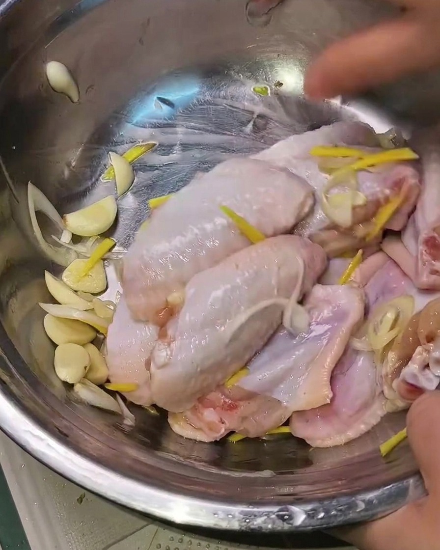 Mains mélangeant les ailes de poulet marinées avec les aromates dans un bol en métal.