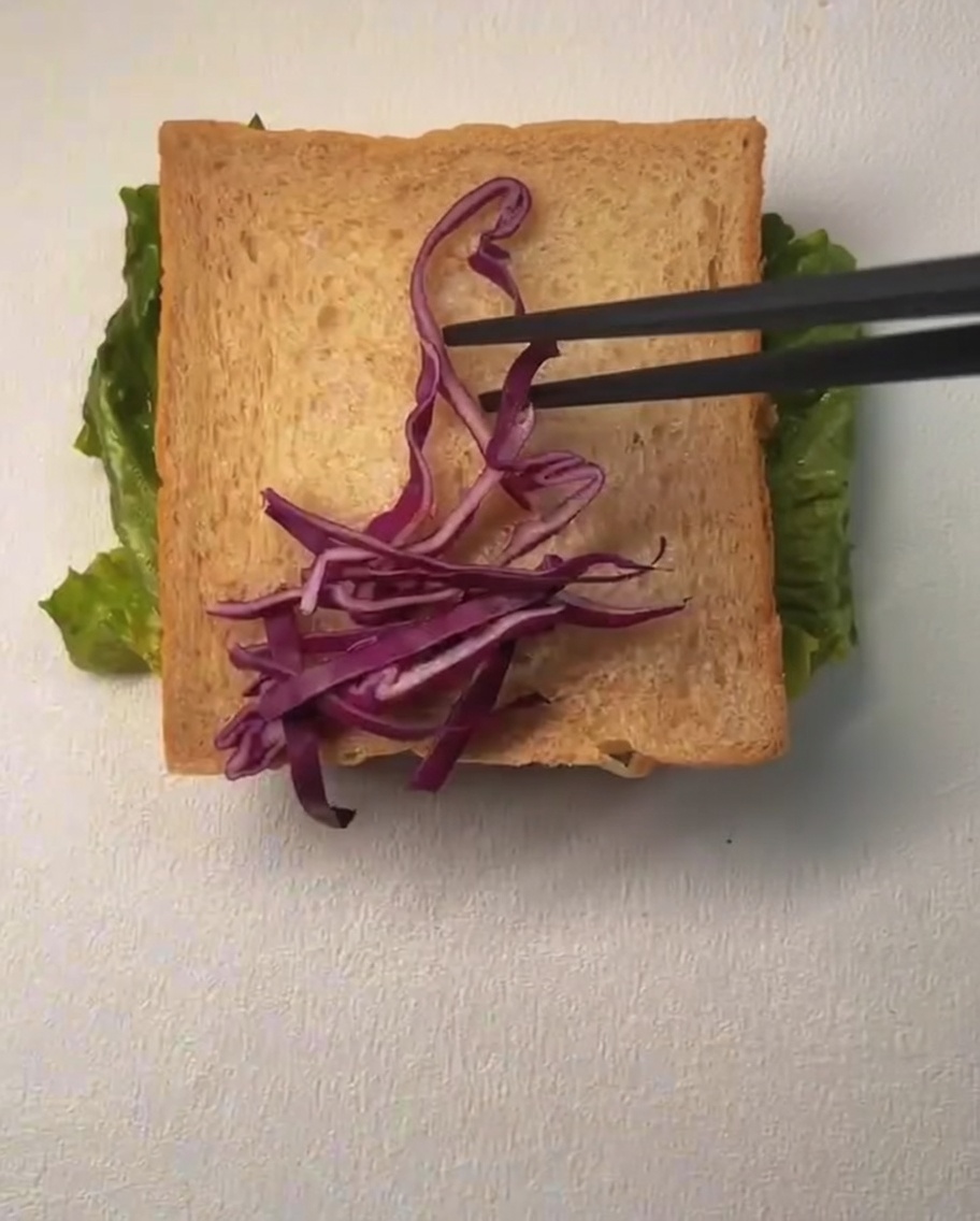 Une tranche de pain garnie de chou rouge râpé et de maïs, avec un filet de mayonnaise sur le dessus.