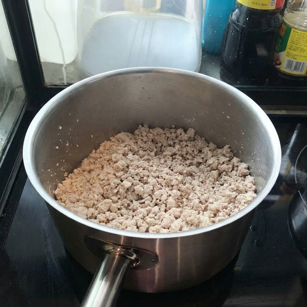 Porc haché qui dore dans une casserole en inox, remué avec une spatule.