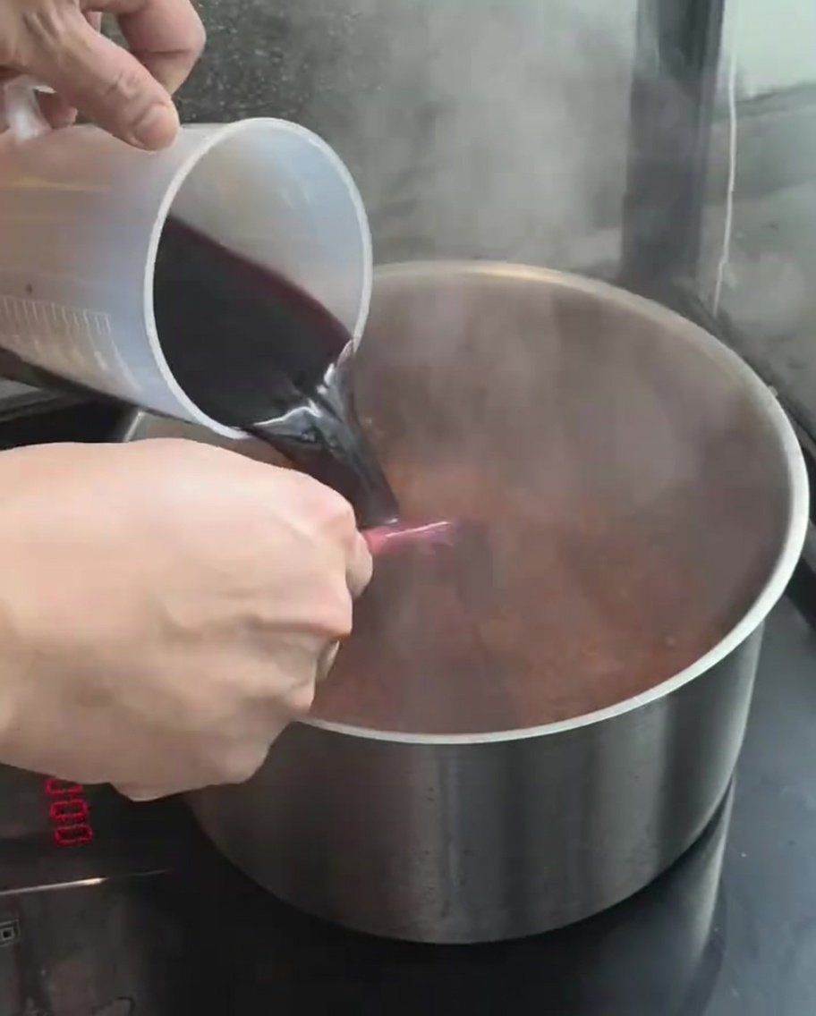 Vin rouge versé depuis un verre doseur dans la casserole.