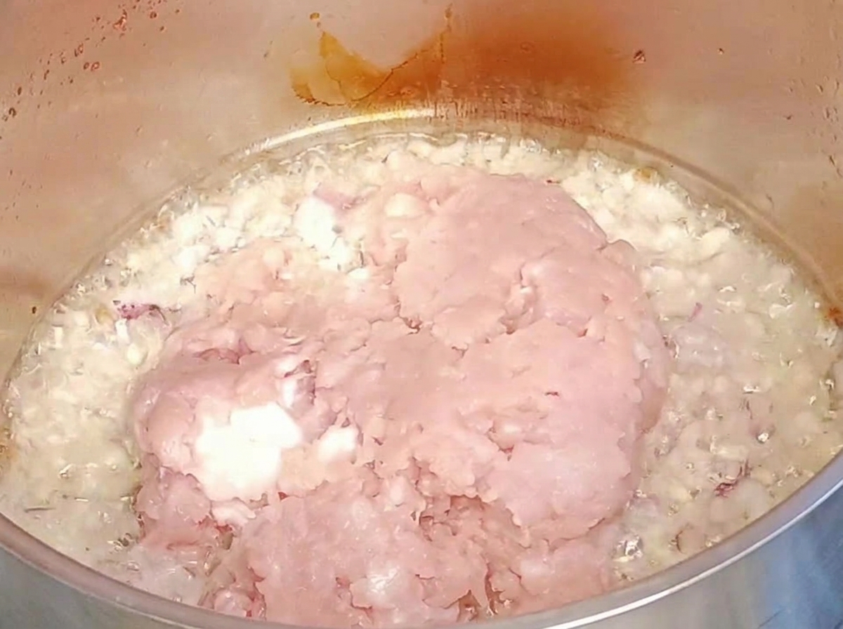 Viande hachée crue ajoutée sur les oignons et lail dans la poêle.