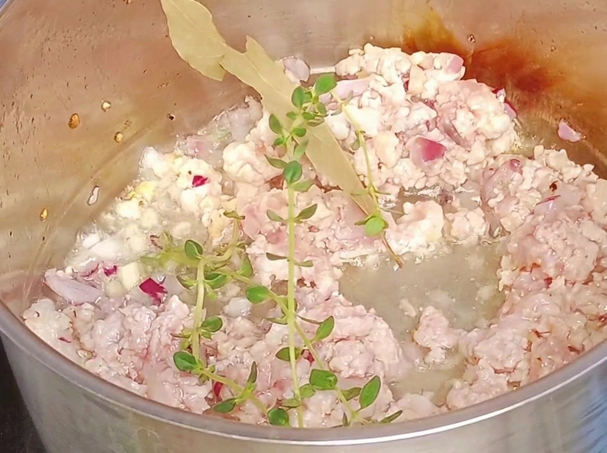 Brins de thym frais et une feuille de laurier ajoutés à la viande dans la poêle.