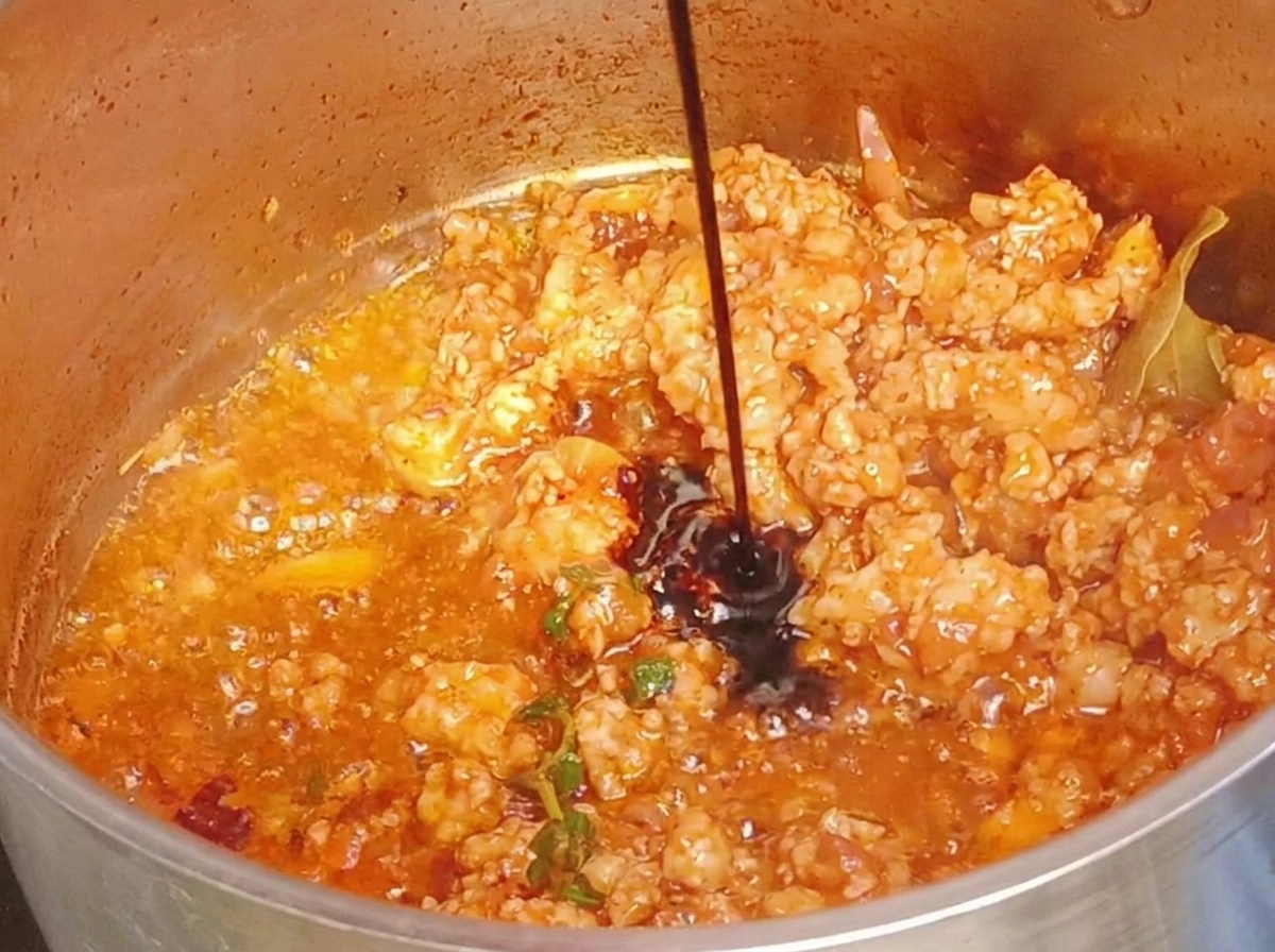 Sauce soja foncée versée sur la viande cuite dans la poêle.