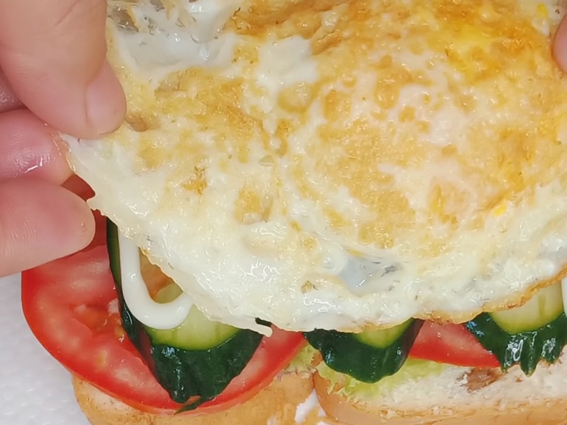 Un œuf au plat parfaitement cuit placé au sommet du sandwich.