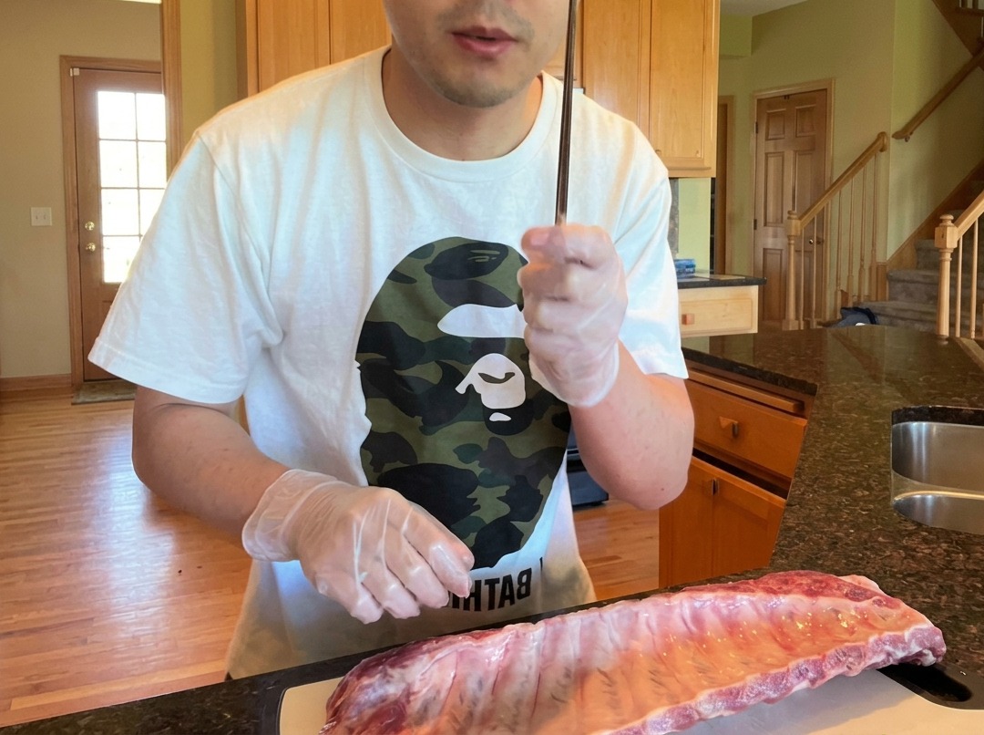 Gros plan montrant une baguette utilisée pour soulever la membrane au dos dun rack de travers de porc crus.