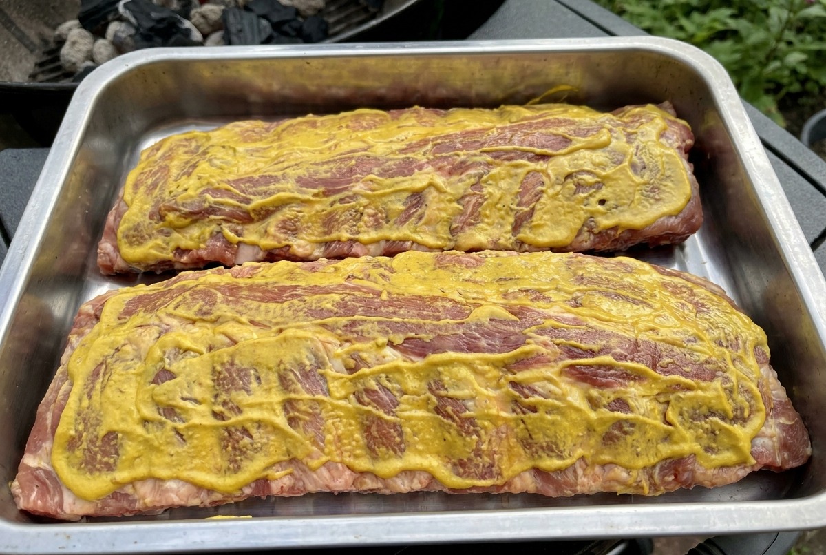 Deux racks de travers recouverts de sauce jaune posés sur les grilles dun fumoir, prêts à être fumés.