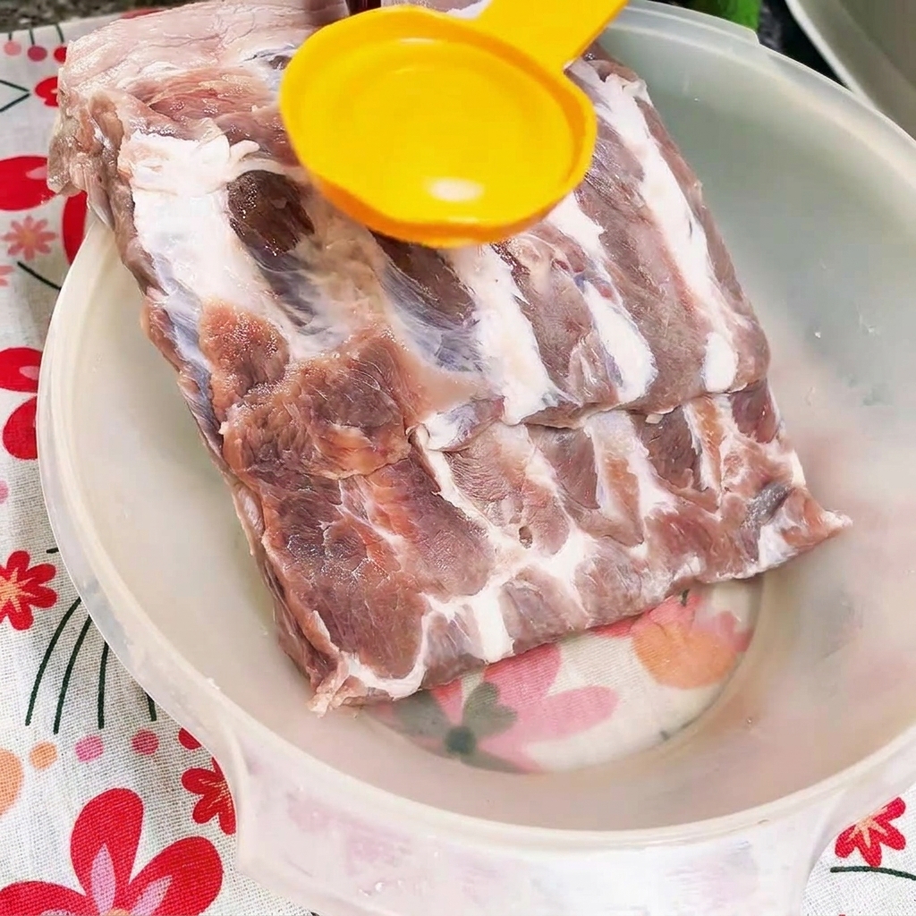 Sauce huître sombre versée sur des travers de porc crus dans un bol blanc.