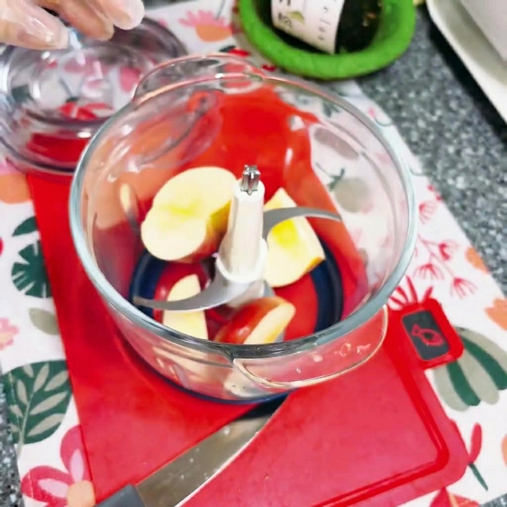 Morceaux de pomme coupés à lintérieur dun petit hachoir électrique en verre.