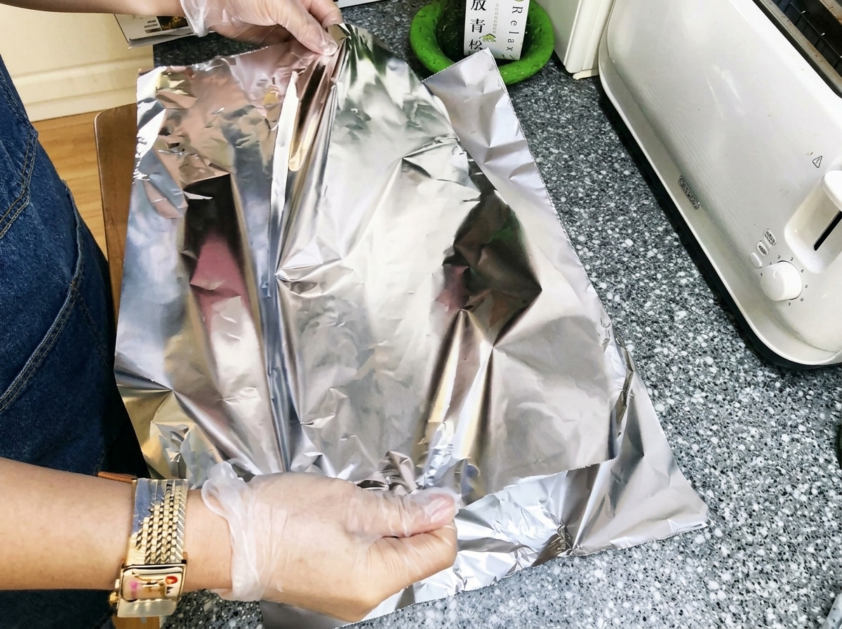 Mains repliant du papier aluminium serré autour des travers de porc marinés pour créer un paquet scellé.