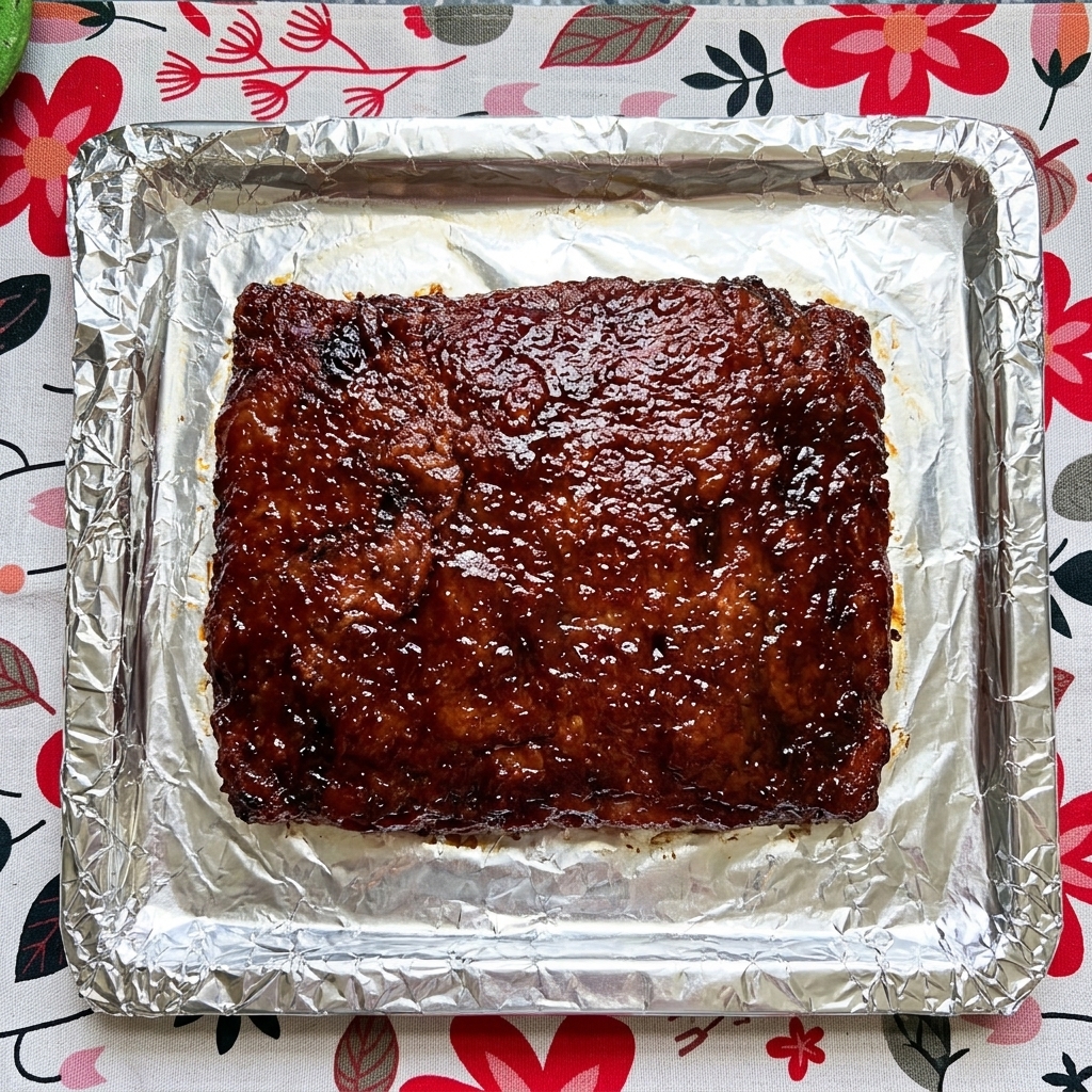 Gros plan sur une plaque de travers de porc cuits sur du papier aluminium, recouverts dune sauce sombre et brillante.