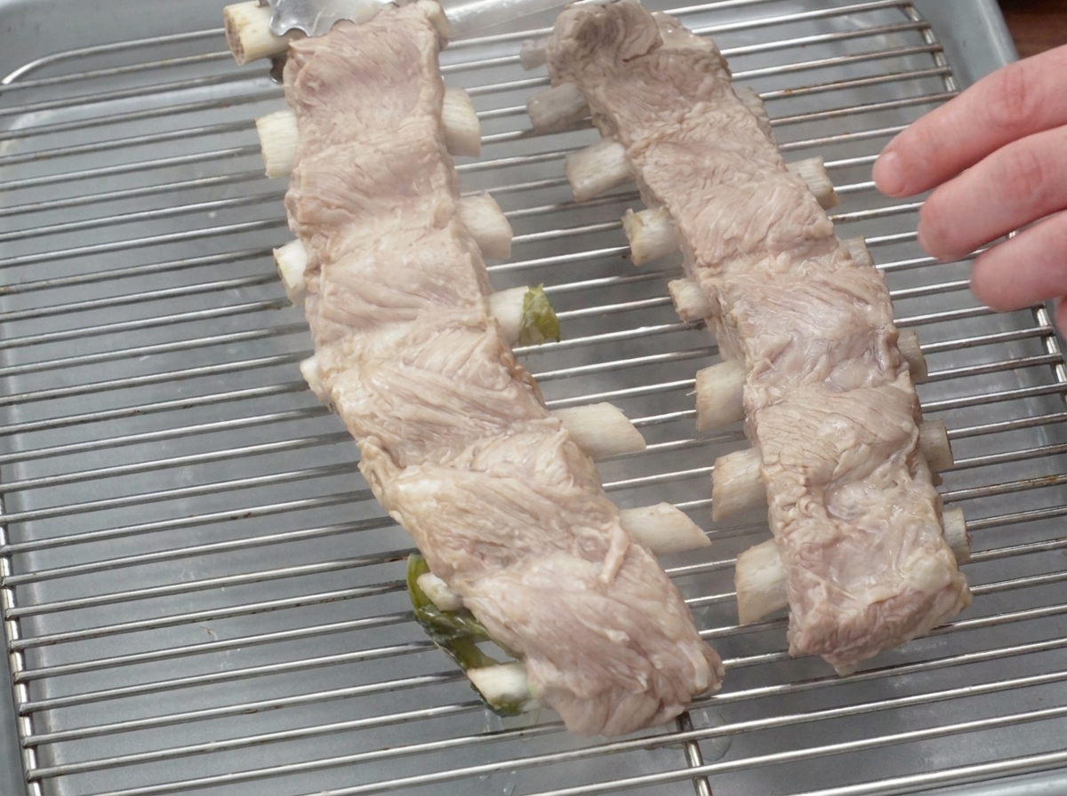 Des racks de travers de porc bouillis reposant sur une grille métallique avec une assiette posée dessus pour les aplatir.