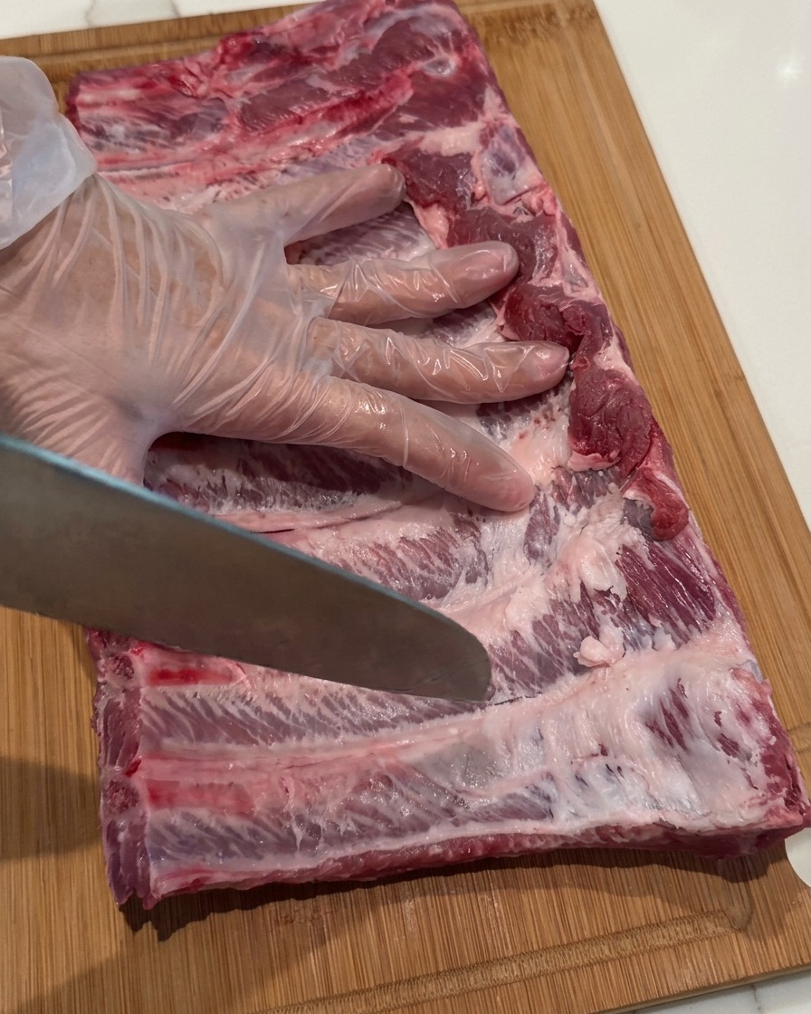 Une main gantée utilisant la pointe dun couteau pour pratiquer de légères incisions sur les travers de porc.