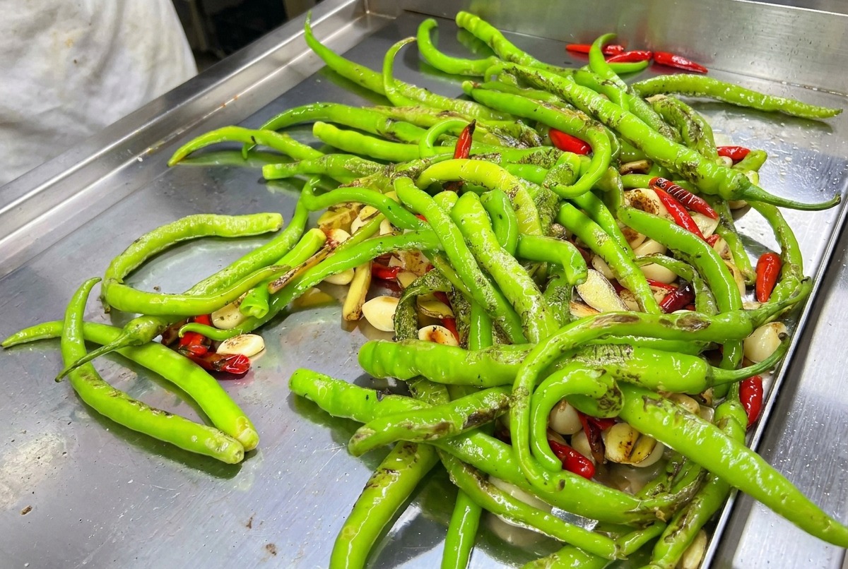 Mélange de piments verts et rouges brûlés au chalumeau sur une plaque chaude.