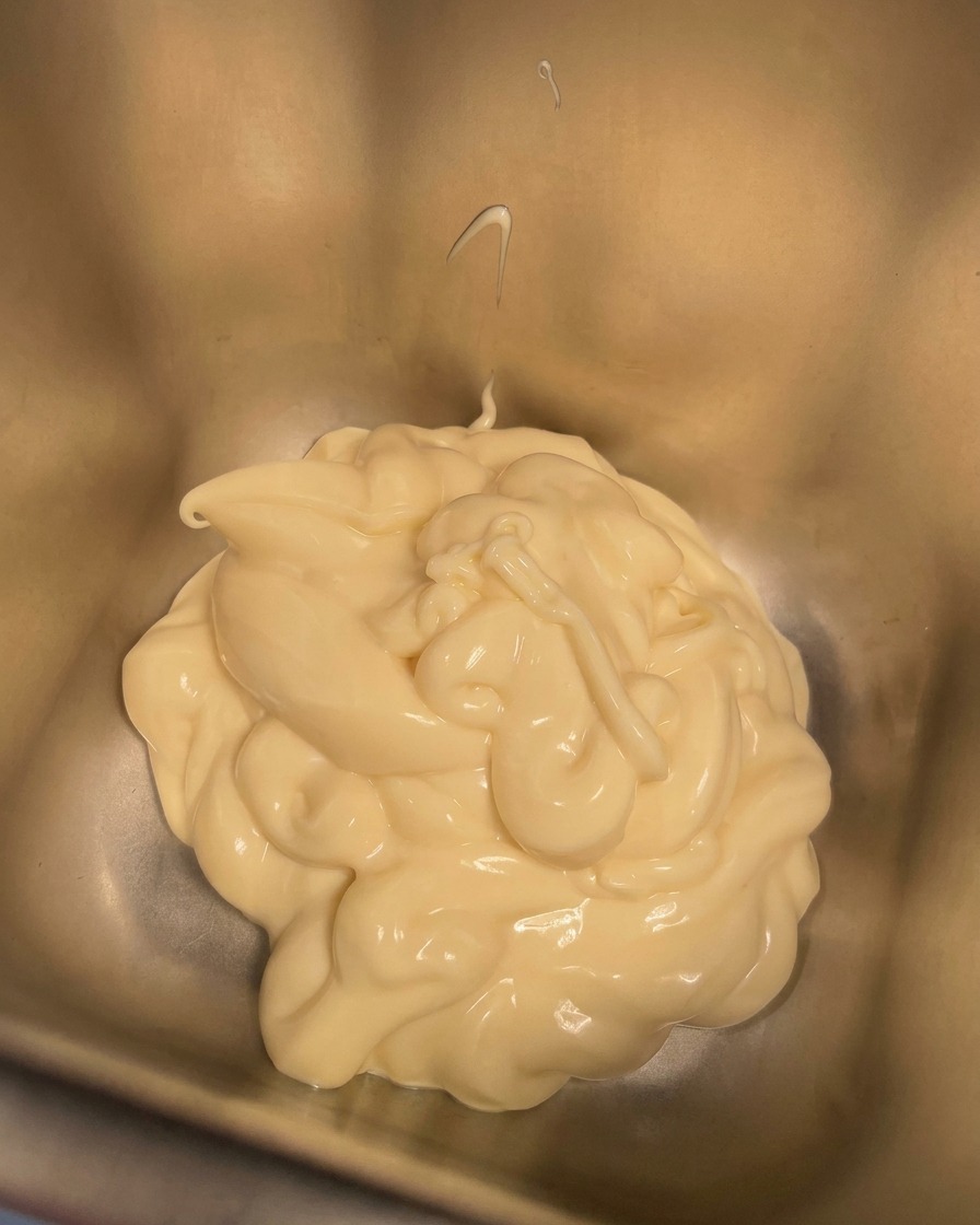 Un petit bol de crème versé dans un récipient contenant déjà la mayonnaise crémeuse.