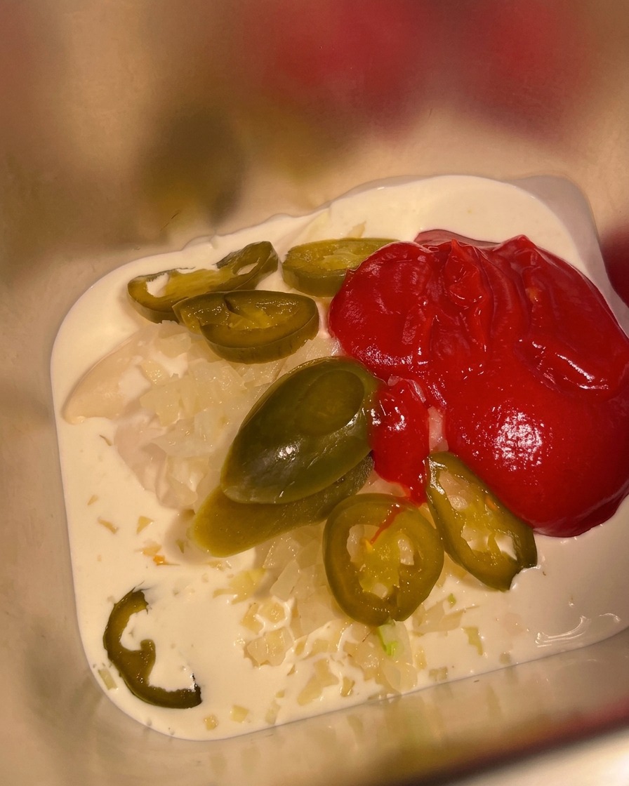 De la sauce piquante mexicaine versée dans le récipient avec la base de crème et mayonnaise.