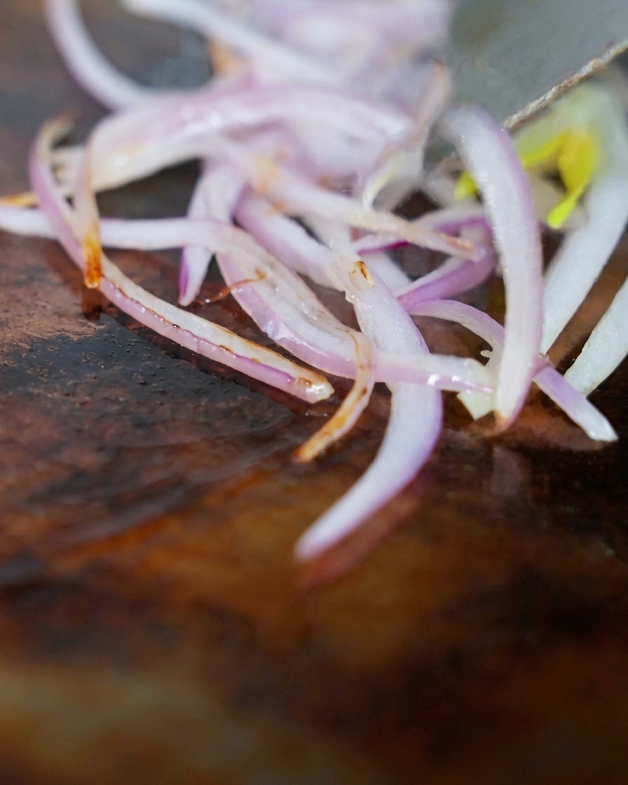 Émincés de poitrine de bœuf Angus et oignons rouges sautant sur une plancha chaude.