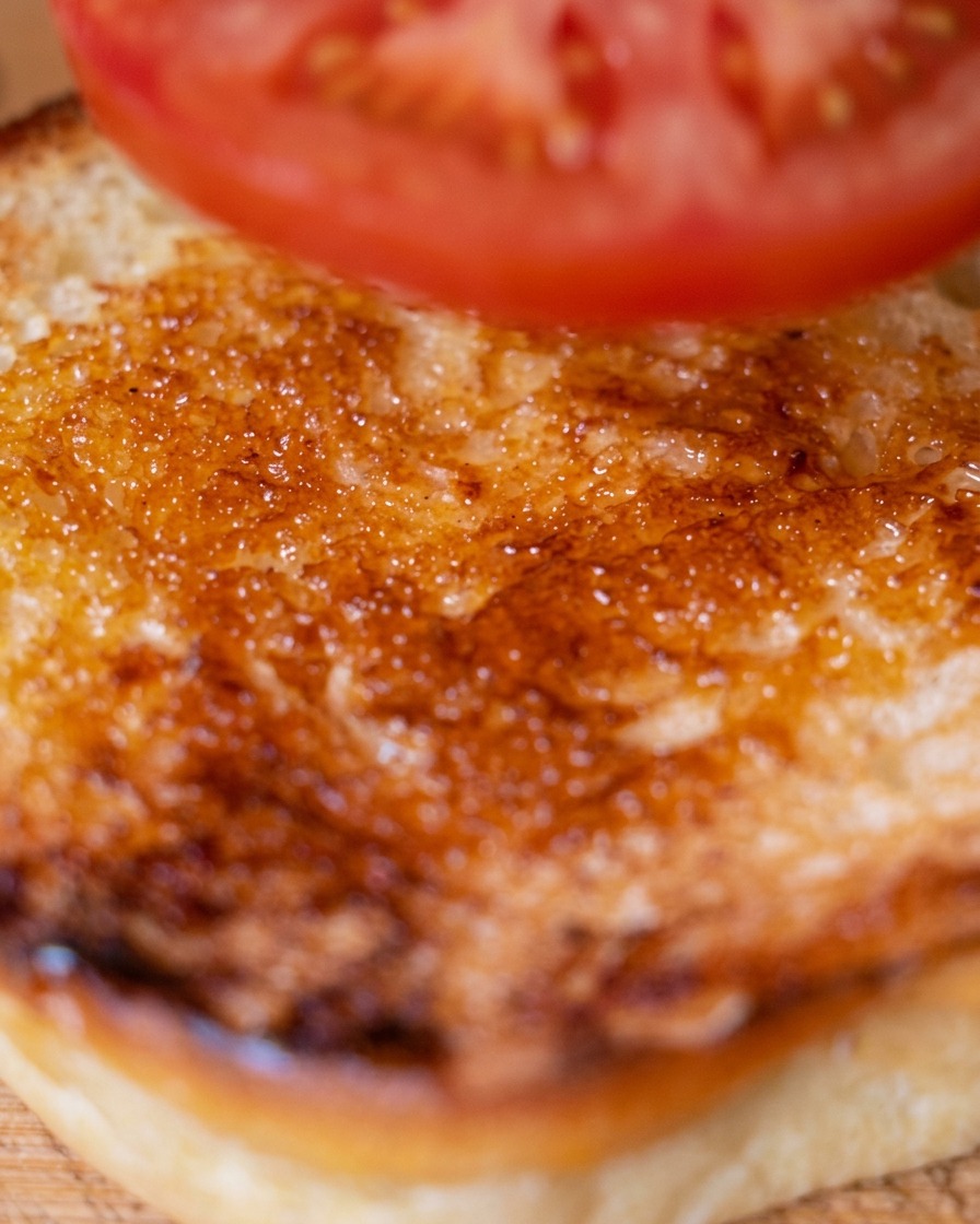 Une tranche de tomate fraîche placée sur la partie inférieure du pain burger toasté.
