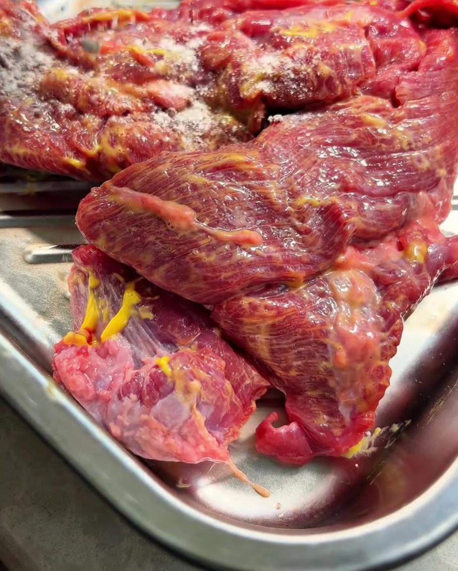 La poitrine de bœuf enduite de moutarde dans un plateau en métal, saupoudrée dépices sèches.