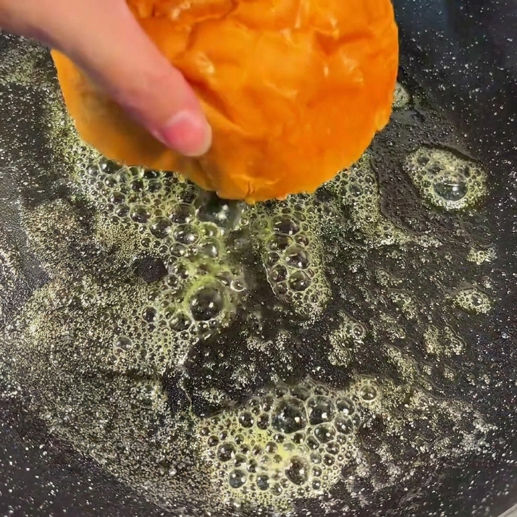 Moitiés de pains à burger face coupée vers le bas dans une poêle contenant du beurre fondu, en train de dorer.