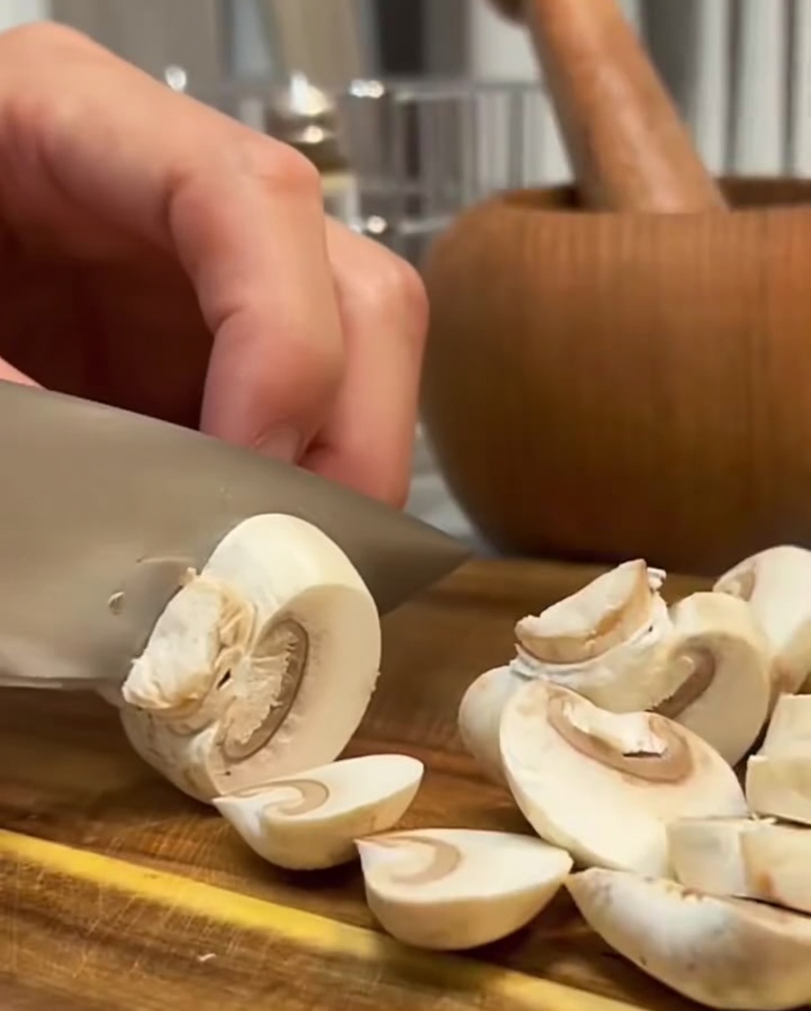 Champignons frais coupés en tranches avec un couteau sur une planche en bois.