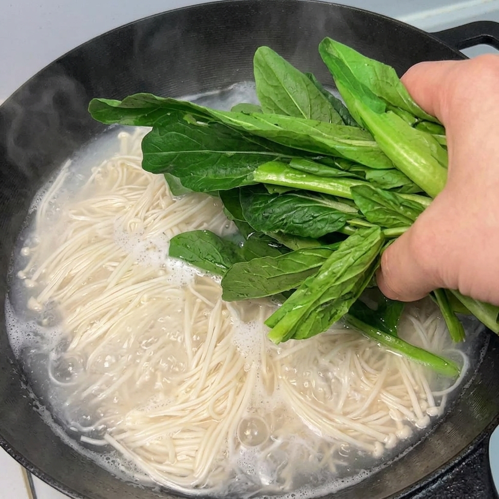 Des légumes verts frais ajoutés dans une casserole de nouilles bouillantes.