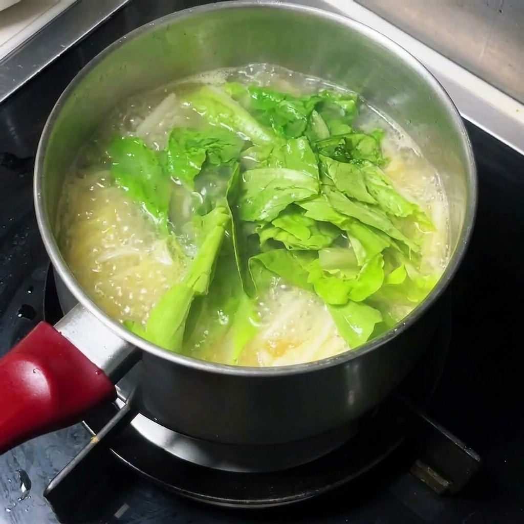 Légumes verts frais ajoutés dans une casserole de soupe de nouilles bouillante.