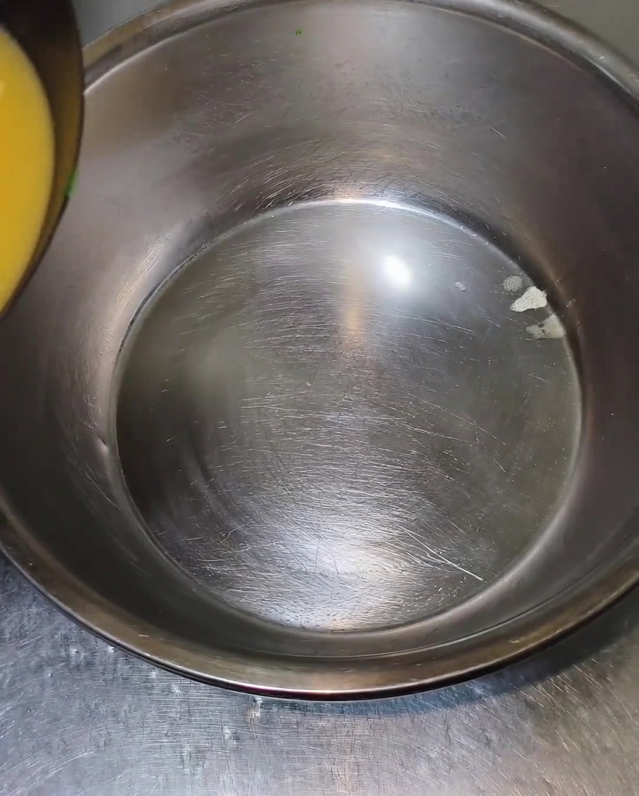 Du bouillon chaud et jaunâtre est versé sur le bord dun grand saladier en acier inoxydable vide.