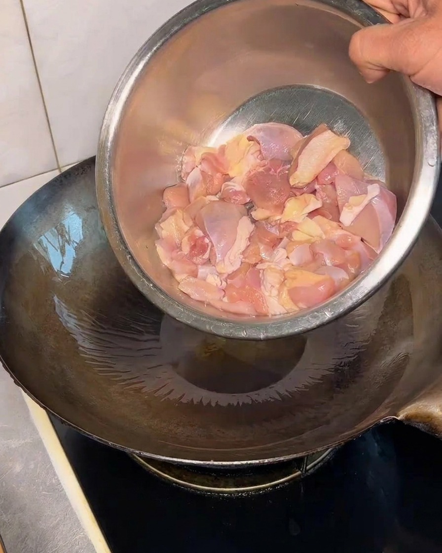 Morceaux de poulet ajoutés dans un wok chaud huilé.