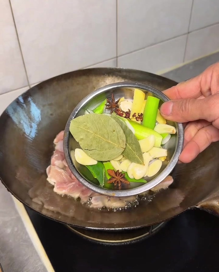Divers aromates entiers ajoutés au poulet dans le wok.