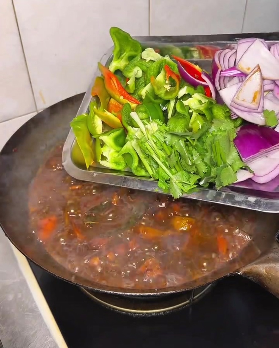Poivrons, oignons et coriandre ajoutés au ragoût de poulet.