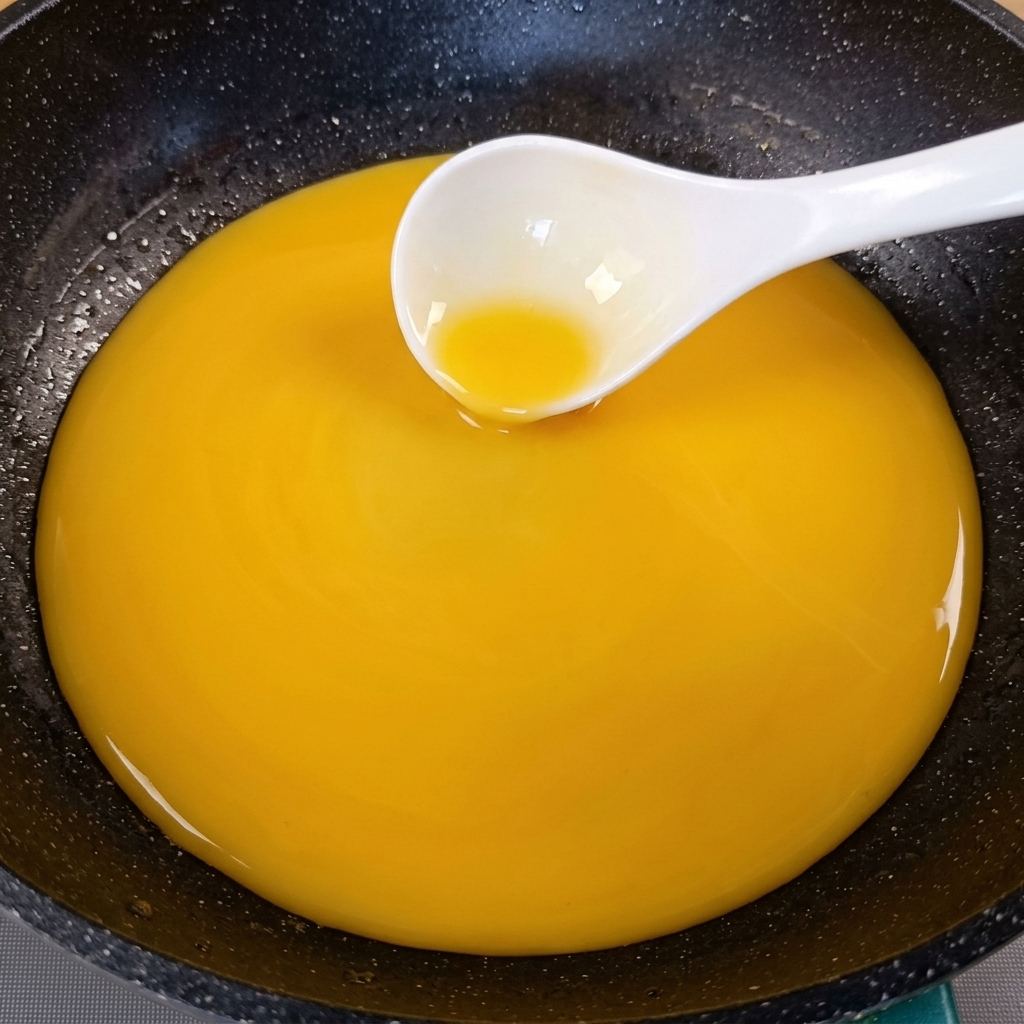 Une sauce jaune doré épaissie remuée dans une poêle sombre avec une louche blanche.