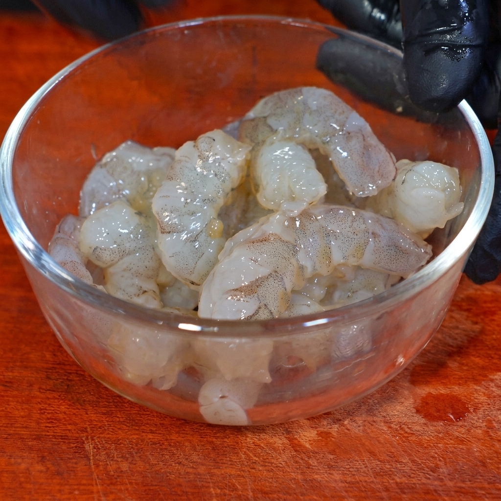 Crevettes marinant dans un bol en verre avec assaisonnement et fécule.