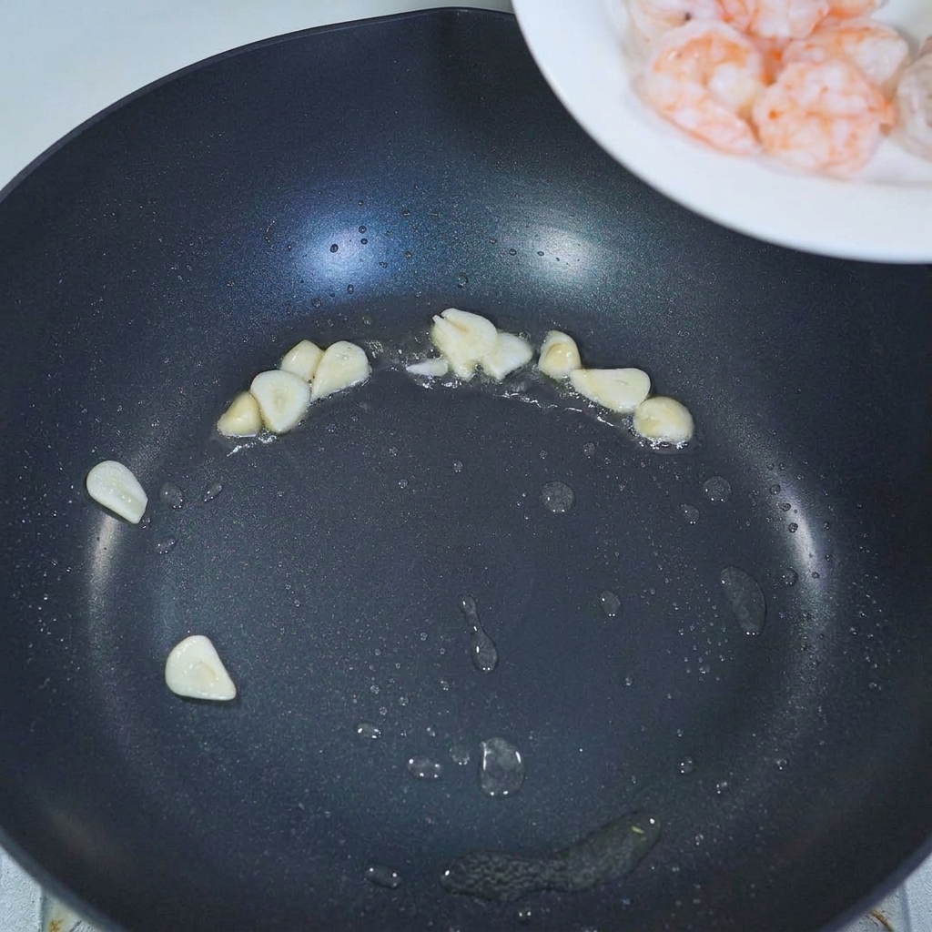 Crevettes précuites ajoutées à une poêle avec de lail sauté.