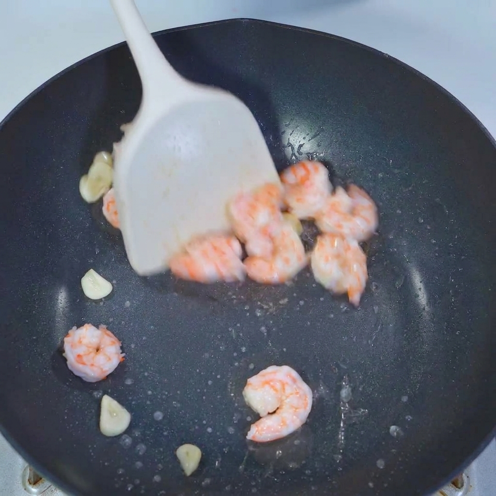 Morceaux de gombo mélangés dans une poêle avec crevettes et ail à laide dune spatule.