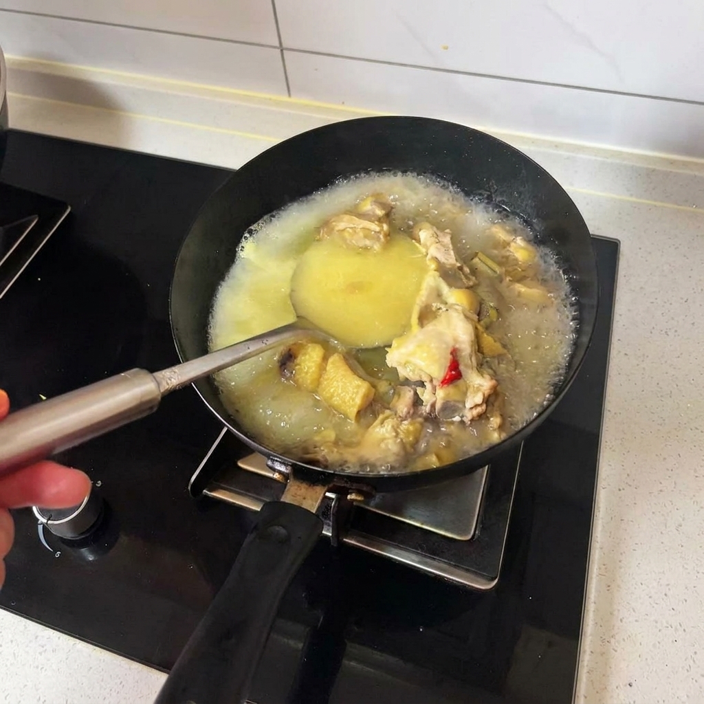 Une louche remuant du bouillon de poulet doré brûlant et des morceaux de poulet cuits dans un wok noir.