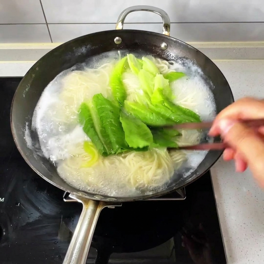 Des nouilles fines et des légumes verts frais bouillonnant dans un wok deau, remués avec des baguettes en bois.