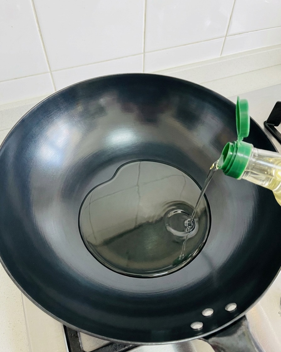 Huile dolive versée dans un wok sombre, vide et chaud.