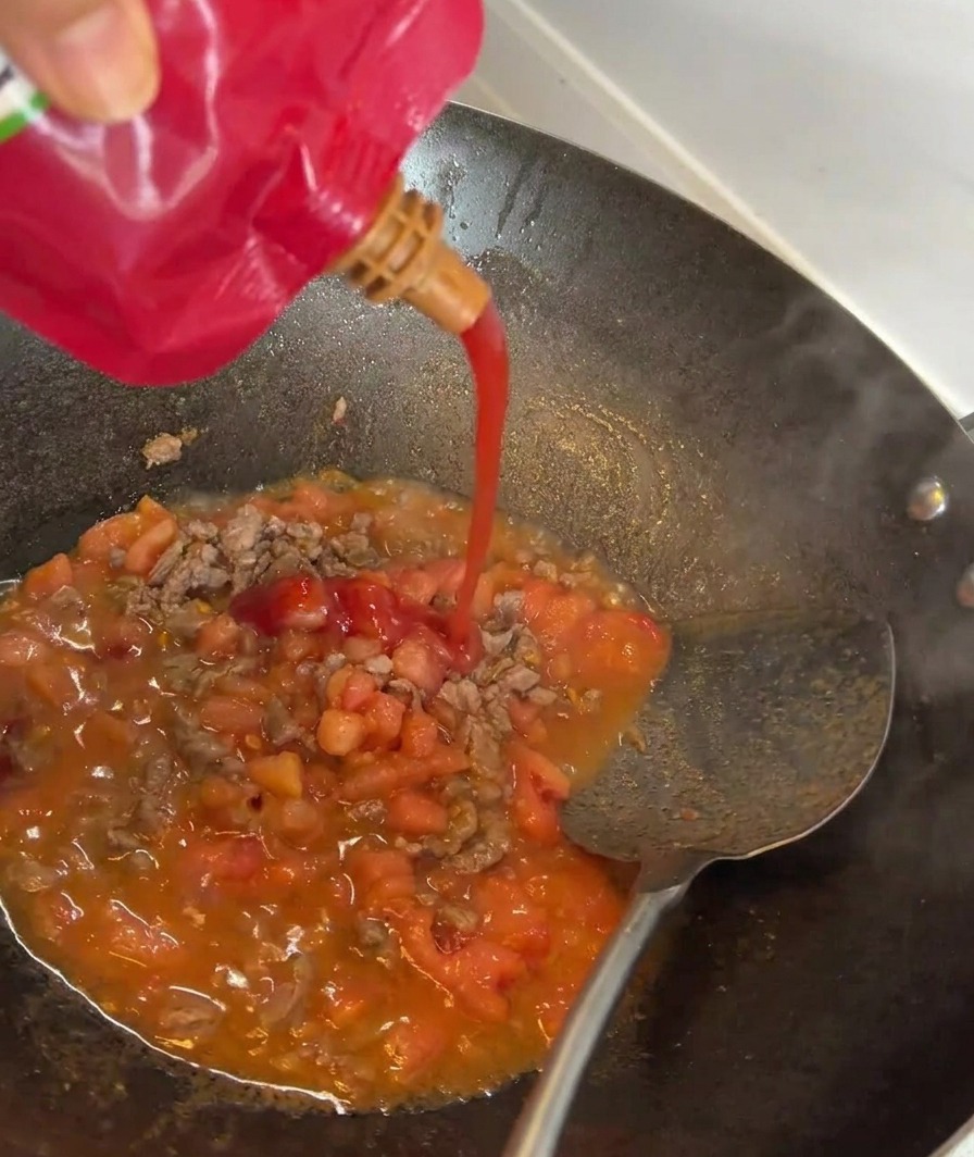 Concentré de tomate versé dans une poêle avec le bœuf et les tomates sautés.
