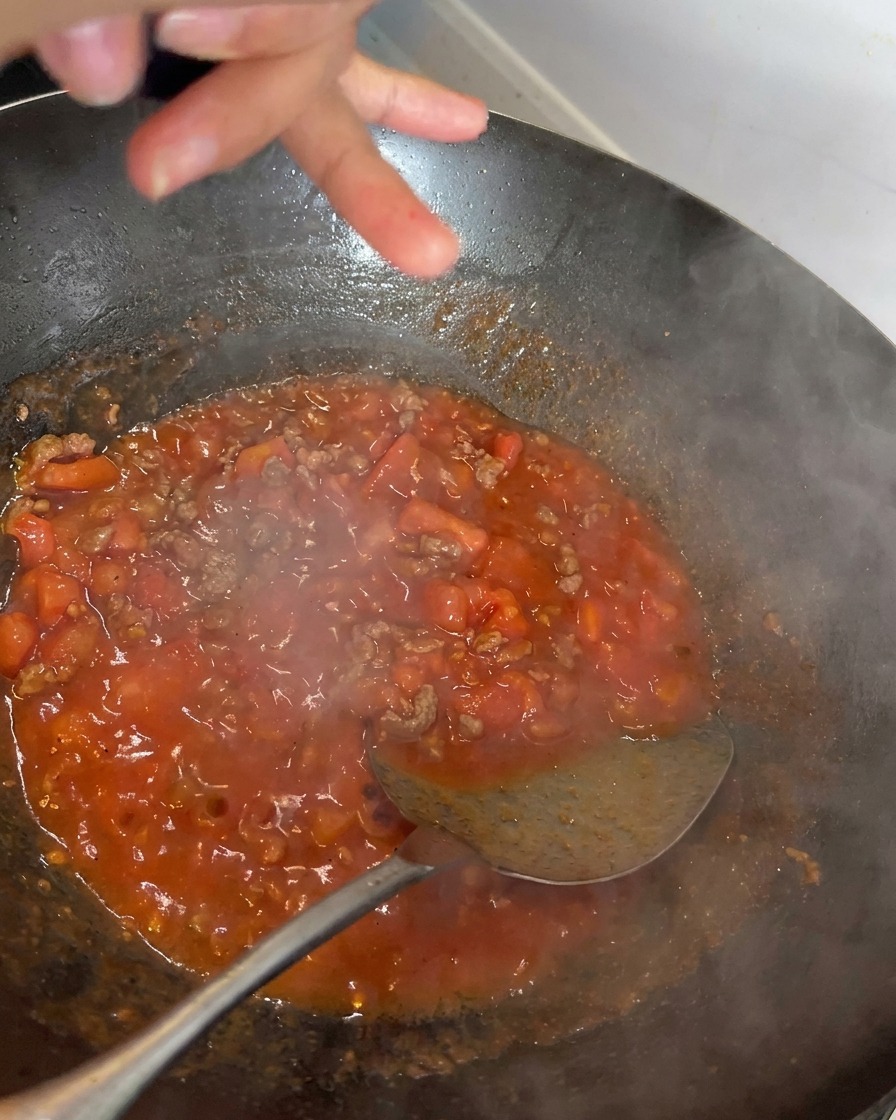 Poivre noir fraîchement moulu sur une riche sauce rouge frémissante à base de tomates et de bœuf dans un wok.