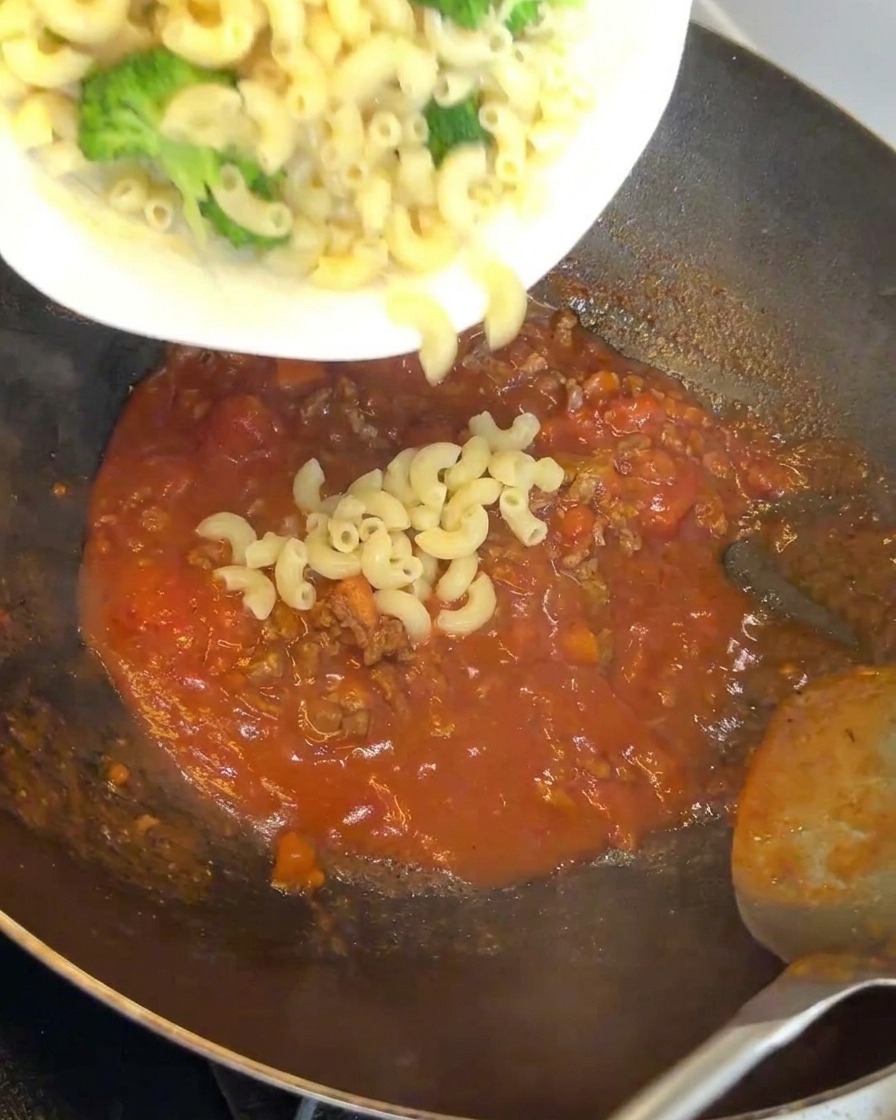 Macaronis et brocolis ajoutés à un wok rempli dune sauce savoureuse à la viande rouge.