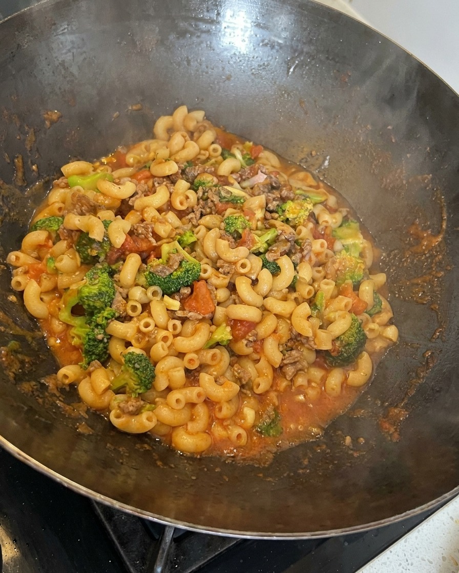 Pâtes, bœuf, brocoli et fromage fondant remués ensemble dans un grand wok.