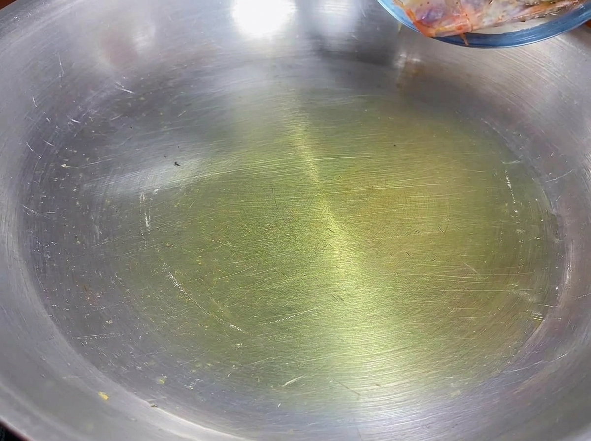 Têtes de crevettes saisies dans de lhuile dolive dans une poêle en inox.
