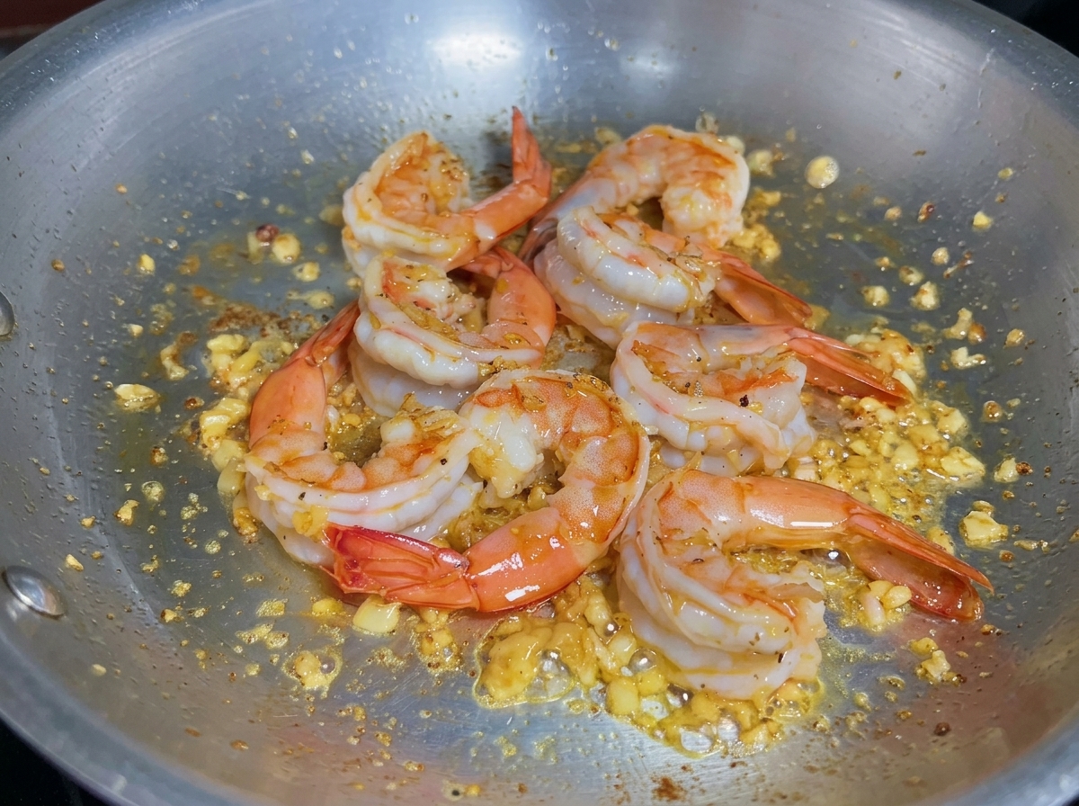 Liquide versé dans une poêle avec des crevettes cuites pour déglacer et récupérer les sucs.