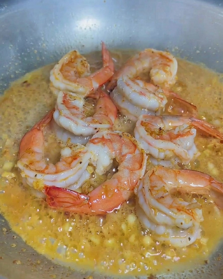 Crème versée dans une poêle contenant les crevettes et lail.