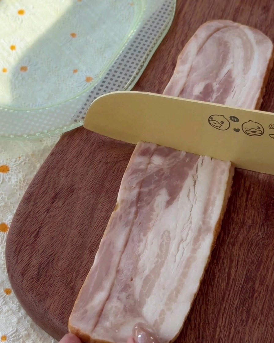 Tranches de bacon cru coupées en morceaux uniformes sur une planche en bois.